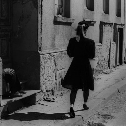 Eine Frau ist von hinten zu sehen, die durch eine dunkle Gasse läuft (Schwarzweiß-Bild).